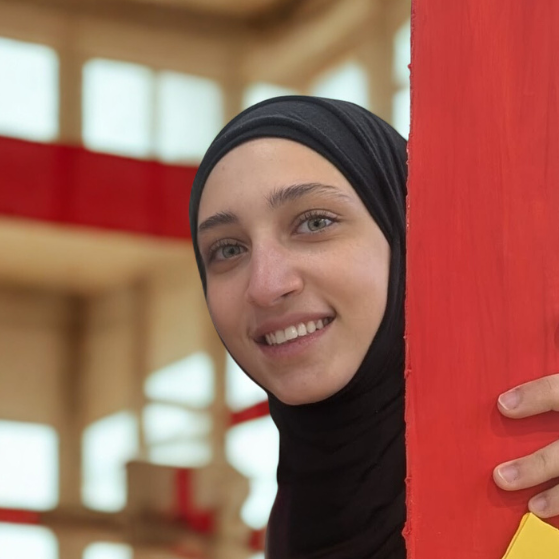L'entraîneuse des Little Kickers, Aya, se tient à côté d'un pilier rouge.